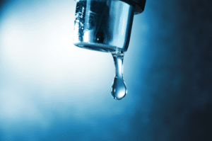 Water dripping down from faucet on color background, closeup